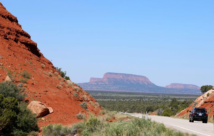 A car drives down the Bicentennial Highway with the two bluffs known as the "Bears Ears" standing off in the distance in the Bears Ears National Monument in Utah.