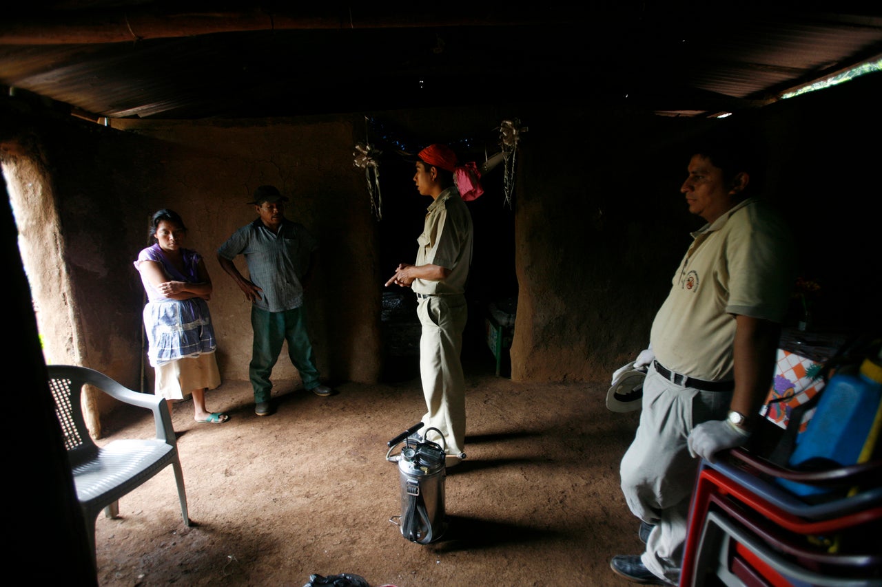 Guatemalan health inspectors speak to a family before fumigating their adobe hut, which is infested with kissing bugs.