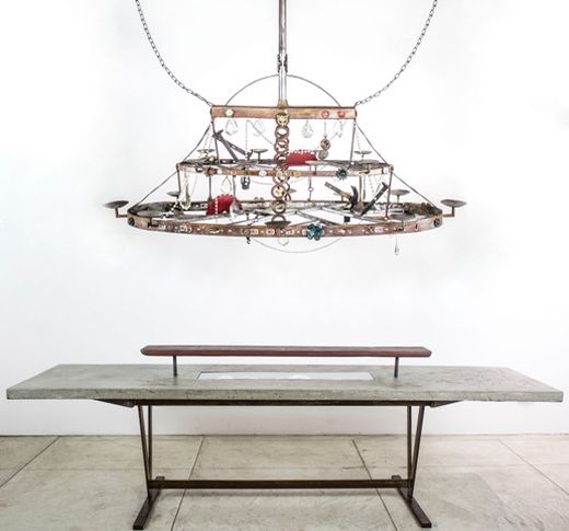 <p><em>“12 guests garden table” by</em><strong> </strong>Flavio Alejandro Bisciotti Metal base concrete top, electrical fixture and broken china 28”x108”x29” + <em>“20 Candles garden Chandelier” </em> by Flavio Alejandro Bisciotti Two tier candle chandelier. Materials from the fire 63”x26”x58”</p>