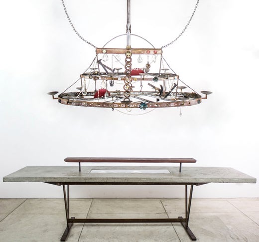 “12 guests garden table” by Flavio Alejandro Bisciotti Metal base concrete top, electrical fixture and broken china 28”x108”x29” + “20 Candles garden Chandelier”  by Flavio Alejandro Bisciotti Two tier candle chandelier. Materials from the fire 63”x26”x58”