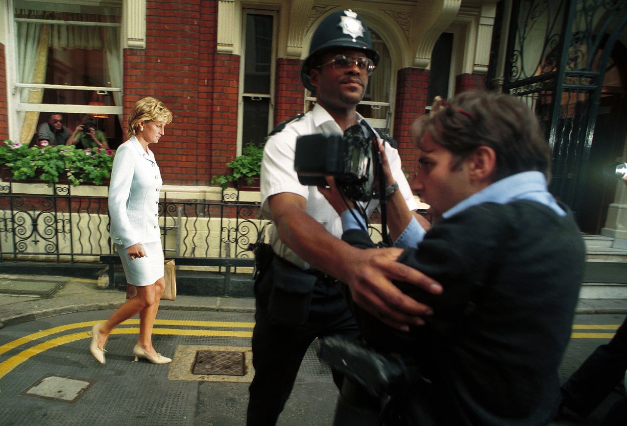 Princess Diana, on the day of her divorce from the Prince of Wales was announced, with a policeman holding back a photographer.