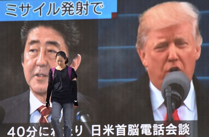 A woman walks in front of a huge screen displaying Japanese Prime Minister Shinzo Abe (L) and US President Donald Trump (R) in Tokyo