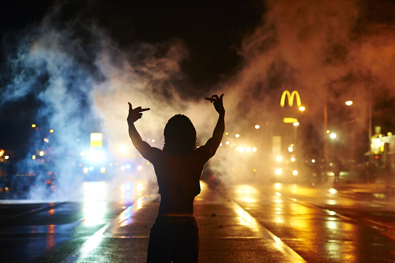 A protester gestures angrily at cops as tear gas fills the streets of Ferguson after curfew early Sunday, Aug. 17, 2014.