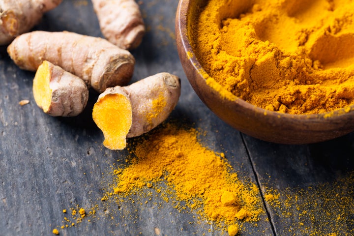 Fresh turmeric roots and turmeric powder in a wooden bowl. 