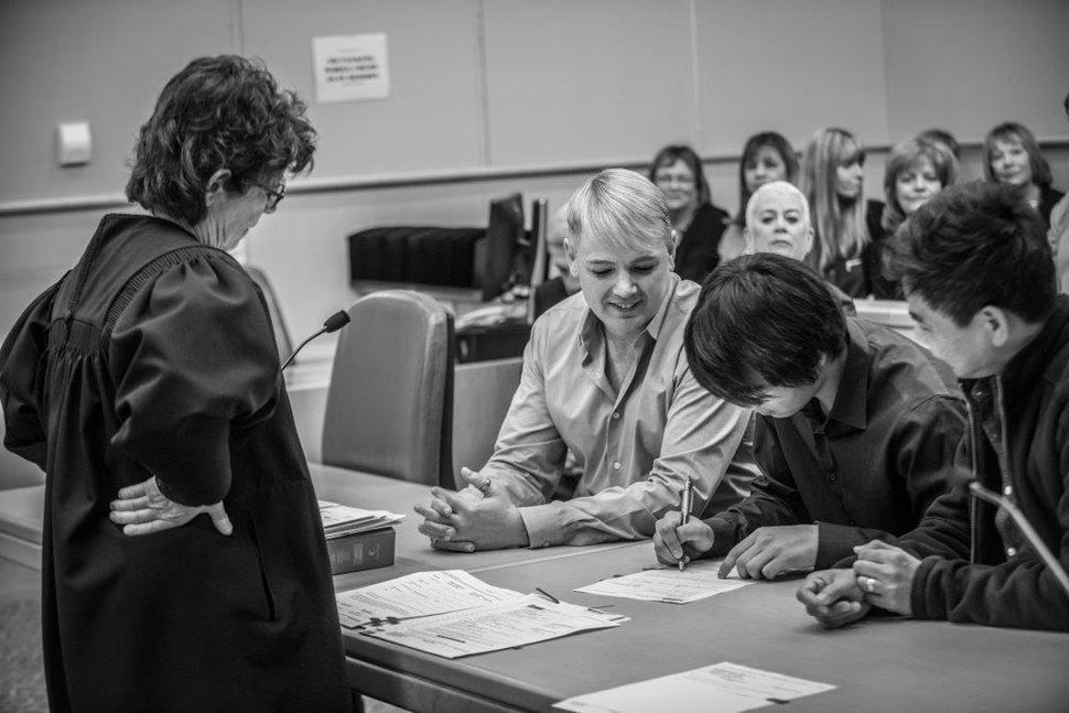 Judge Marta Diaz watches over as Tom Bauer (left) and his husband, Nilo Ventura (far right) sign the adoption papers with Jon Cardoza.