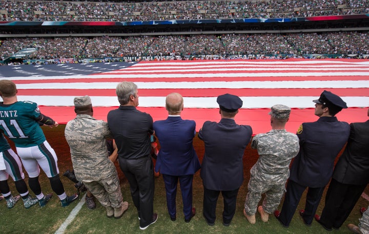 Vice President Joe Biden (blue suit), Philadelphia Eagles head coach Doug Pederson (left), and members of the military and police help hold a large American flag before a 2016 game.