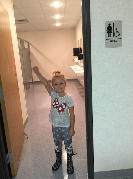 Emma raises a triumphant fist in the girls' bathroom at her new school.
