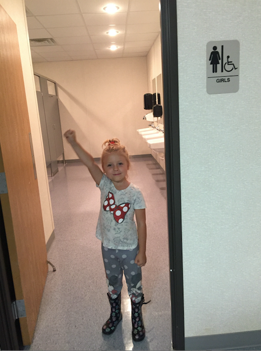 Emma raises a triumphant fist in the girls' bathroom at her new school.