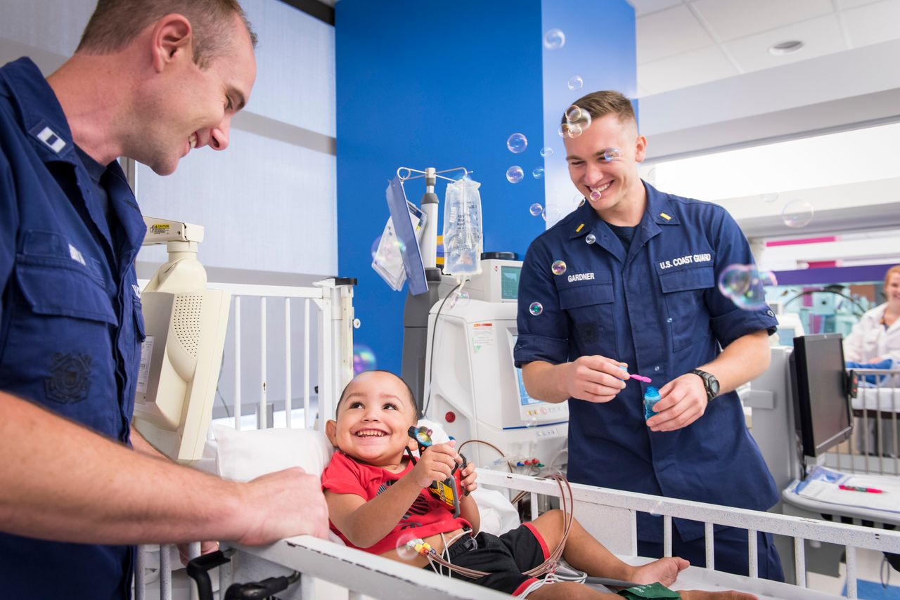 Coast Guard Lt. Brad Bryan (left) and Ensign James Gardner play with Zaiden Thomas, a dialysis patient who the two Guardsmen helped rescue during the floods caused by Hurricane Harvey. On Labor Day, the pair met some of the patients they delivered to Texas Children's Hospital in Houston and the staff with whom they coordinated the missions.