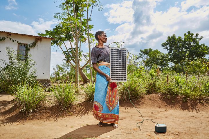 Violet Napazi, 57, holds up the solar panel owned by her son, Master, Luchenza, southern Malawi, 2017. Charging mobile phones is becoming a profitable business, especially since solar panels are becoming cheaper to buy and build. Until recently, Violet’s family used the solar panel to charge a battery which was then to used charge mobile phones. But since the inverter burnt out, it can only power one phone at a time. 