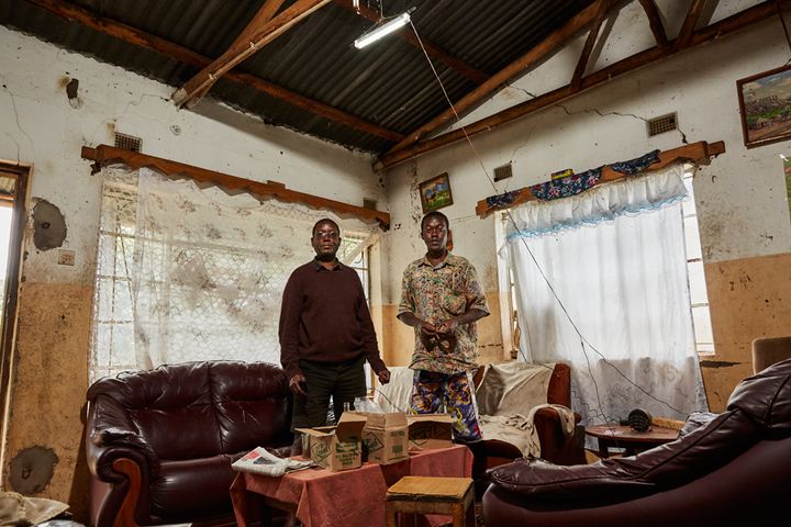 Robert Wonga (56), and his son Felix (29) stand in the living room of their home, Luchenza, southern Malawi, 2017. The solar panels that Felix uses for his mobile phone charging business also powers their lights, and several small radio’s and speakers. Felix: “We are the only ones in this area that have a charging business. If more people in this area had solar panels it would very much improve their lives. ESCOM [the national provider], is too expensive and not reliable.”