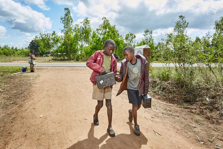 From left to right: Jan Chumba (12) and his brother Ben (10) carry two solar batteries home, after picking them up at Green Malata, an entrepreneurial training village that offers a variety of green alternatives to Malawi’s notoriously unreliable national electricity provider, ESCOM, Luchenza, southern Malawi, 2017.