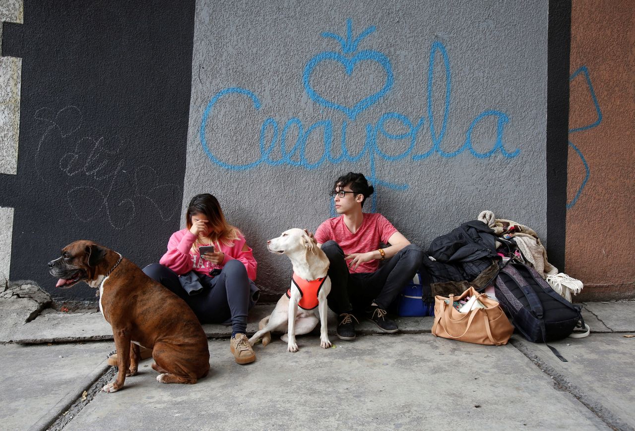 Residents wait with their pets and belongings outside of a damaged building 
