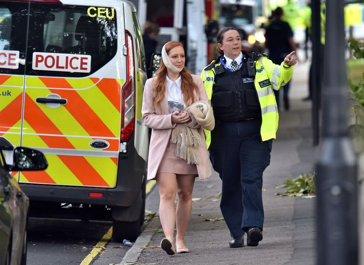 An injured woman is assisted by a police officer close to Parsons Green station