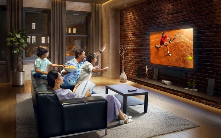 :biggrin:Father and two young children cheering and watching Tennis game on TV. Mother is reading a magazine. They are sitting on a sofa in the modern living room. The TV set is on the loft brick wall. It is evening outside the window. Dmytro Aksonov via Getty Images