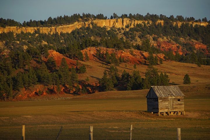 A small shed on a free range outside of Hulett Wyoming. This image was taken as the Sun was getting low in the West, the ‘sweet light’ time. Visible are the red Spearfish Formation sedimentary rock at bottom, the brown Stockade Beaver Shale above it, and finally the Hulett Sandstone at the top that is yellowish tan. The colors are dramatic especially at sunrise and sunset. 