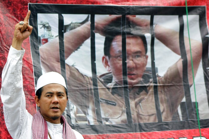 A Muslim protester stands in front of a banner of Ahok outside a courthouse during his trial. Jakarta. Jan. 2017.