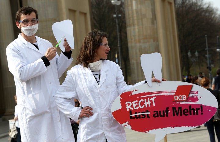 Two demonstrators posing as unequally paid dentists, the woman holding a sign reading 'Not a Wish But a Right to More!', demonstrate during the 'Equal Pay Day' demonstration on March 21, 2014 in Berlin.