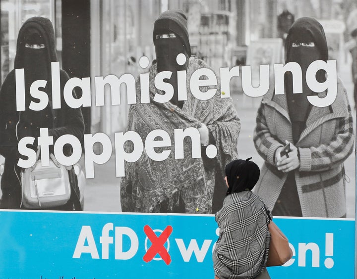 A woman with a headscarf walks past an election campaign poster of the anti-immigration party Alternative fuer Deutschland (A