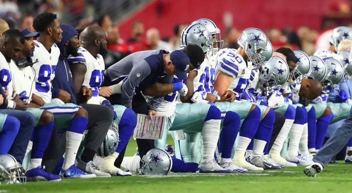 Dallas Cowboys players kneel together with their arms locked prior to the game against the Arizona Cardinals at University of