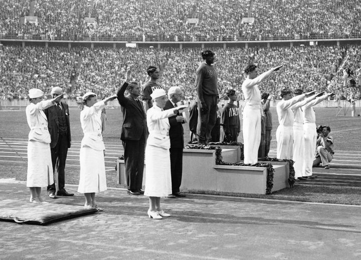 Jesse Owens on the podium at the 1936 Olympics, surrounded by people giving Nazi salutes