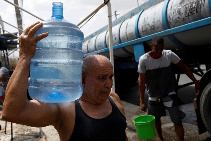 Men carry containers filled with water from a tank truck in the municipality of Canovanas, Puerto Rico, on Sept. 26.