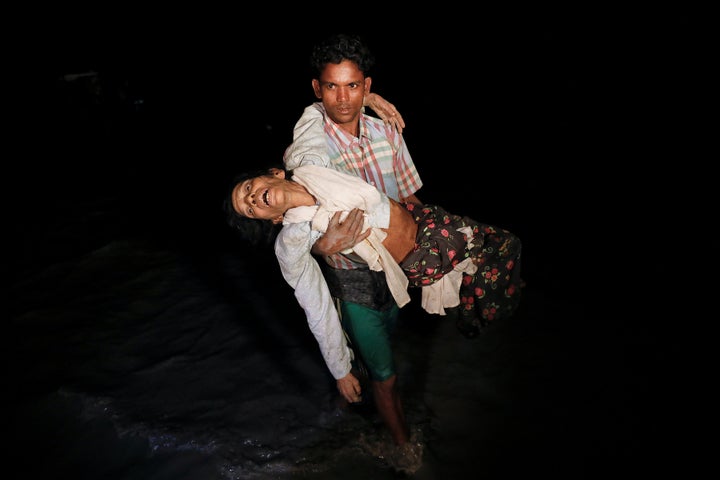 Nobi Hossain wades through the water carrying his elderly relative, Sona Banu, as hundreds of Rohingya refugees arrive by woo