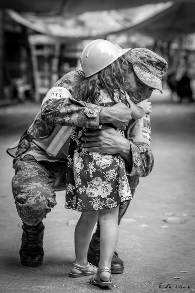 A young girl hugs a man in uniform.
