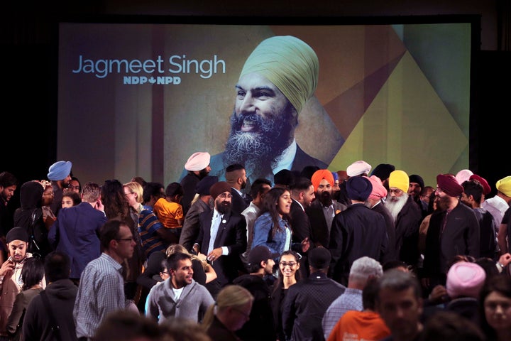 A photograph of Jagmeet Singh is projected on a screen behind a full stage of supporters after Singh won the leadership of th