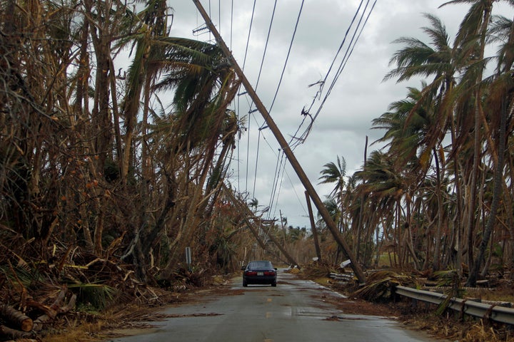 A car drives under tilted power line poles in Humacao, Puerto Rico, in the aftermath of Hurricane Maria.