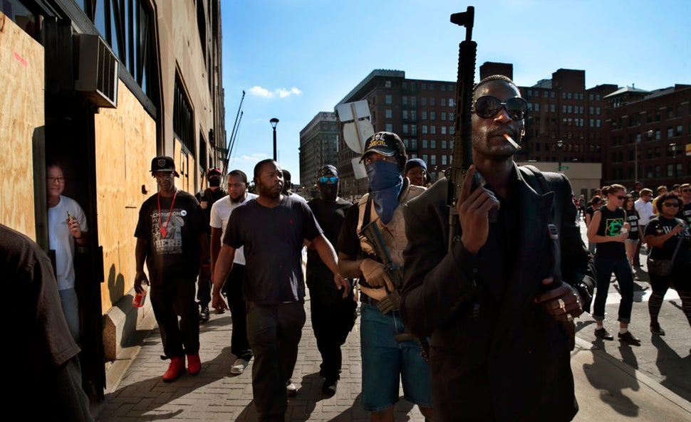 Armed protesters march in downtown St. Louis as a man from a boarded up dry cleaners watches through the doorway after former