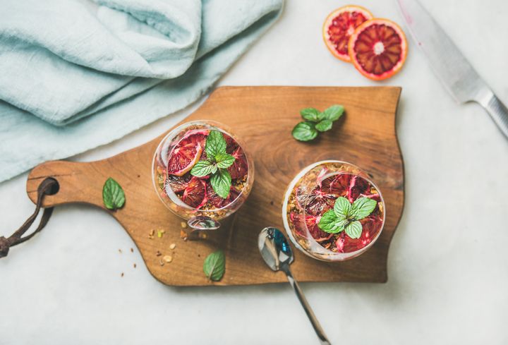 Healthy breakfast. Greek yogurt, granola, blood orange layered parfait in glasses with mint leaves on wooden board over grey marble background, top view. Clean eating, weight loss, detox food concept Foxys_forest_manufacture via Getty Images