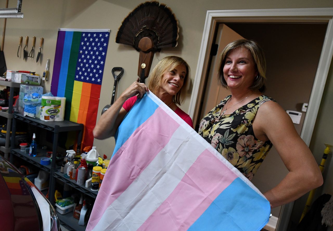 In the garage at their Shawnee home, Suzanne Wheeler and her fiancee, Marsha Riley, show off a transgender flag, with a gay pride flag on the wall.