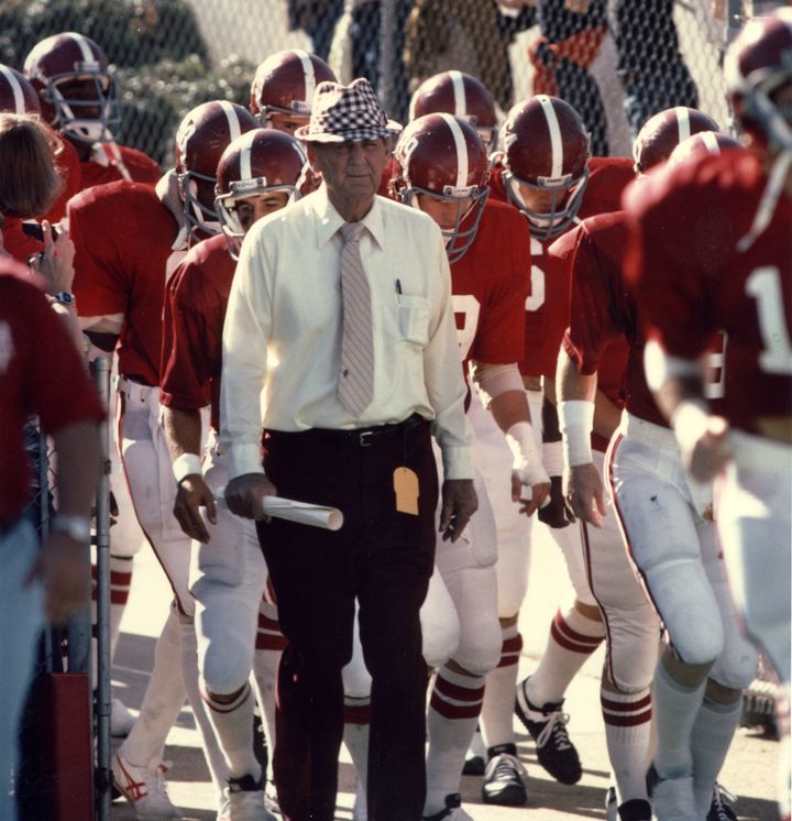 Bryant leading his team onto the field, with his trademark hat and rolled-up papers.