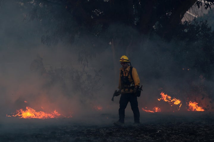 A firefighter works to put out hot spots on a fast-moving, wind-driven wildfire in Orange, California.