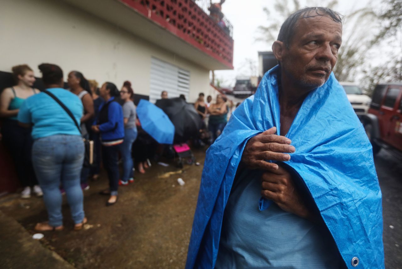 Arian Rodriguez covers himself in a tarp as residents of Juyuya wait in the rain for more than seven hours to register with FEMA.