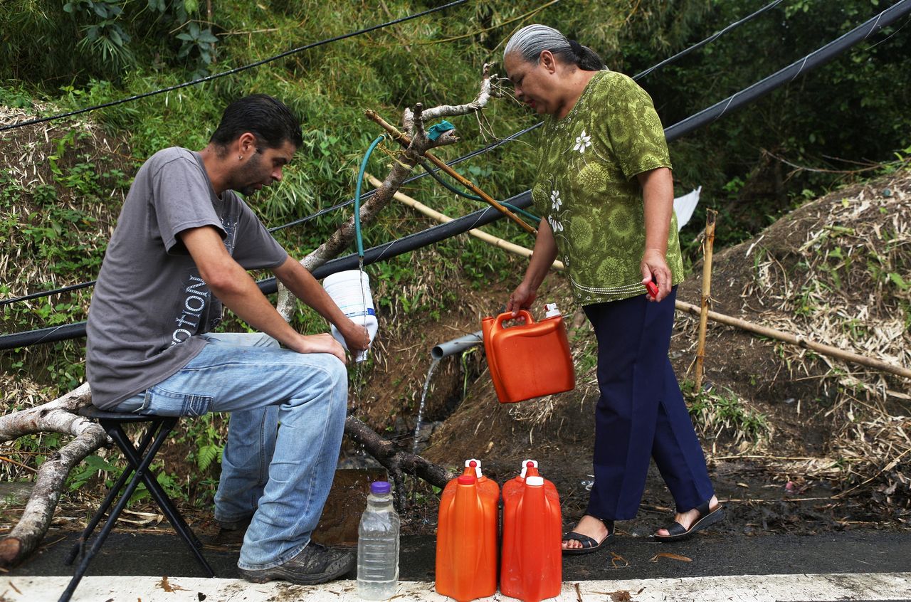 Migdalia Aceuedo and her son collect spring water in Utuado near a downed power line. Their house and much of the town is without running water or power.