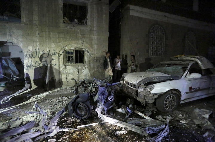 People stand next to wreckage at the site of a car bomb attack in Yemen's capital Sanaa June 29, 2015. A car bomb claimed by Islamic State exploded in the Yemeni capital Sanaa overnight, medics said, wounding at least 28 people gathered to mourn another attack earlier this month.