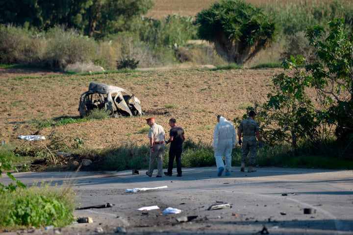 Police and forensic experts inspect the wreckage of a car bomb believed to have killed Caruana Galizia