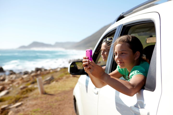 Girl, aged 9, taking a picture of a sea view from a car window Alistair Berg via Getty Images