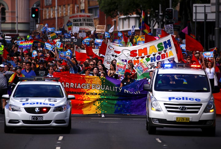 Police drive in front of marchers holding signs and banners as they participate in a marriage equality march in Sydney. 