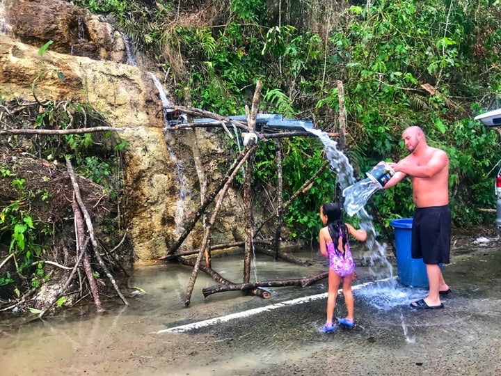 A young girl and her father rinse off in naturally flowing water from the side of a mountain in Ciales, Puerto Rico on Oct. 1