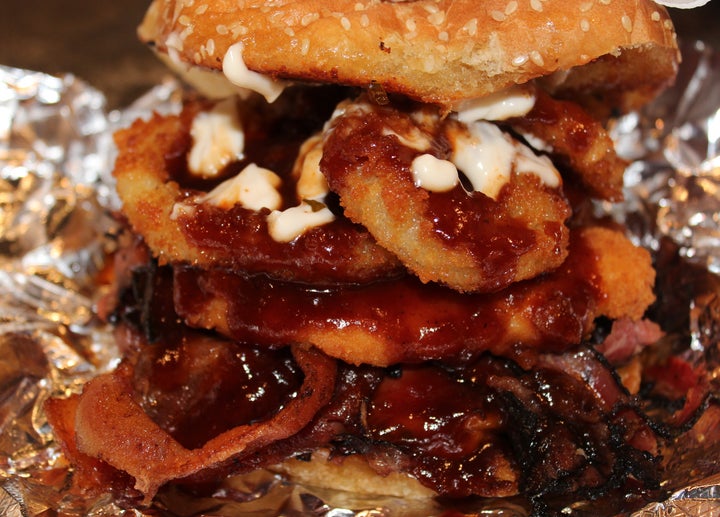 Pastrami Western Burger with melted cheddar, crisp bacon, hot pastrami, chicken fingers, onion rings, honey bbq, mayo, on a garlic buttered bun.