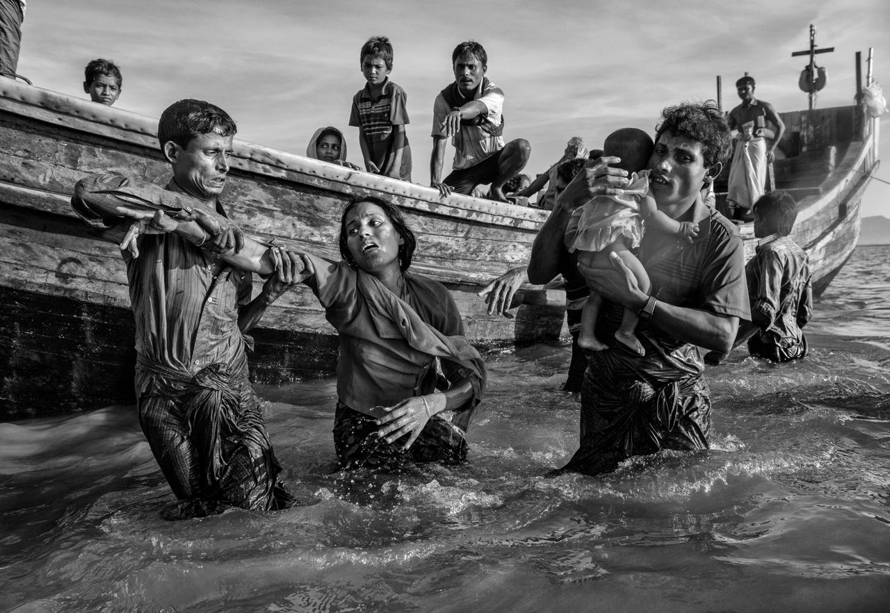A Rohingya refugee woman is helped from a boat as she arrives exhausted on the Bangladesh side of the Naf River after fleeing her village in Myanmar.