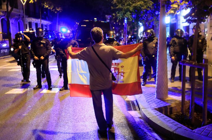 A pro unity demonstrator displays a Spanish flag to Catalan Regional Police officers.
