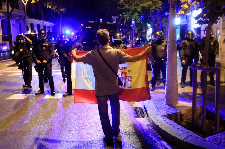 A pro unity demonstrator displays a Spanish flag to Catalan Regional Police officers.