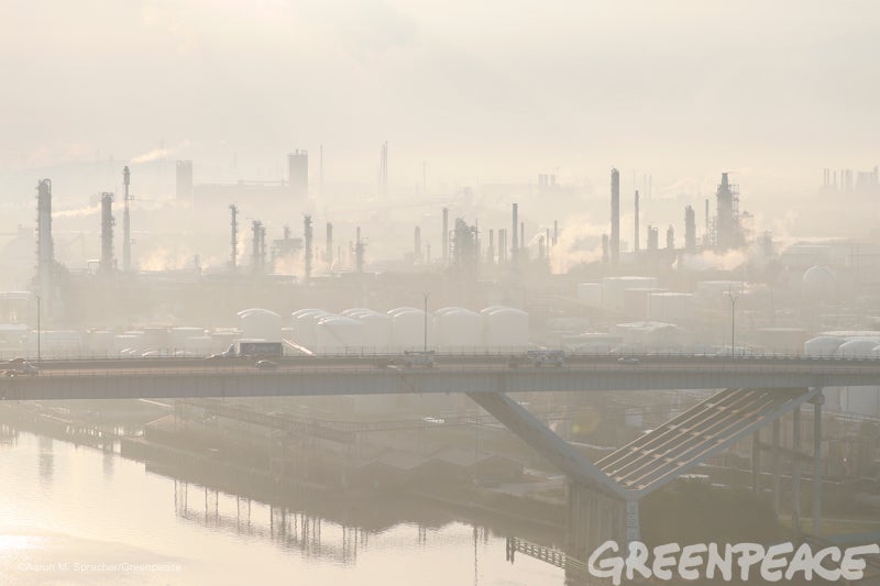 Vehicles make their way across a bridge in haze from the oil refining industrial complex behind them in Manchester, Texas, mo