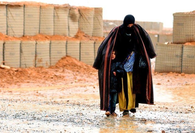 A Syrian refugee from the informal Rukban camp, which lies in no-man’s land off the border between Syria and Jordan, walks in the rain on March 1, 2017. She is sheltering a young child outside a U.N.-operated medical clinic immediately on the Jordanian side. 