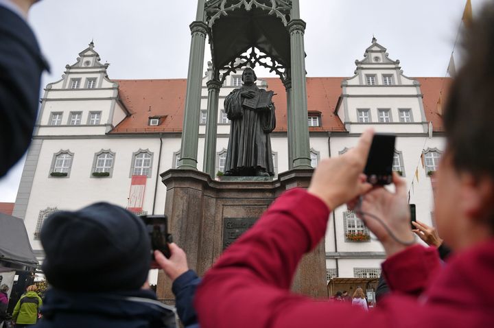 People take pictures of a statue of German Church reformer Martin Luther holding a book including his translation into German of the New Testament of the Bible at the main square in front of the city hall in Wittenberg, eastern Germany, where celebrations take place on the occasion of the 500th anniversary of the Reformation on October 31, 2017. 