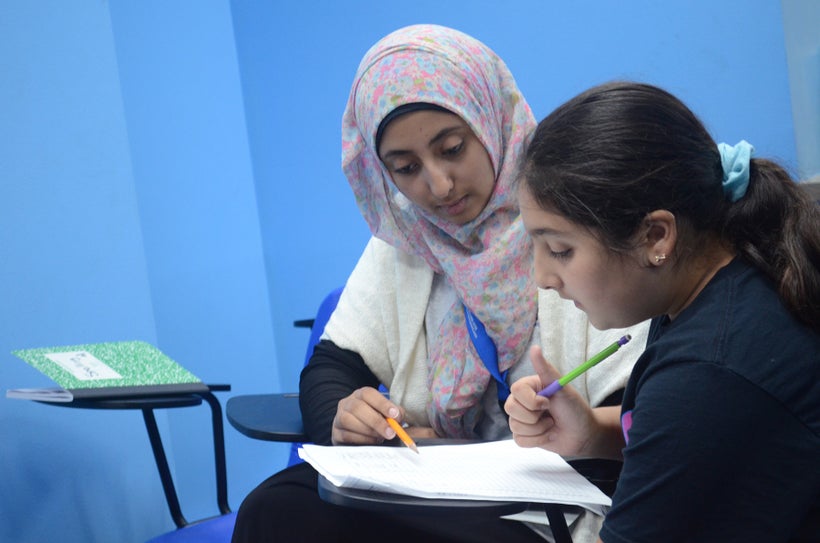 A teenage tutor with Educare helps a young student with her homework.